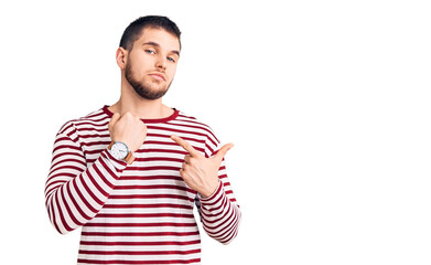 Young handsome man wearing striped sweater in hurry pointing to watch time, impatience, looking at the camera with relaxed expression