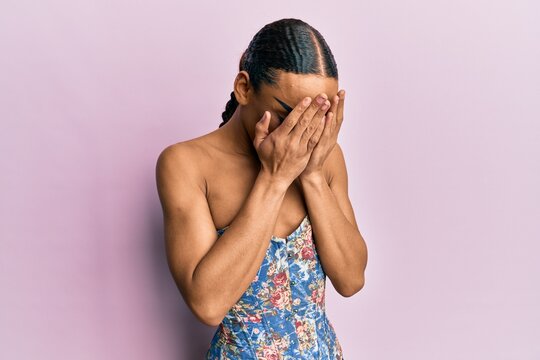 Hispanic Man Wearing Make Up And Long Hair Wearing Elegant Corset With Sad Expression Covering Face With Hands While Crying. Depression Concept.