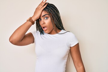 Fototapeta premium Young african american woman with braids wearing casual white tshirt surprised with hand on head for mistake, remember error. forgot, bad memory concept.