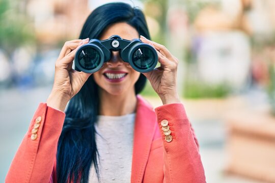 Young beautiful businesswoman smiling happy looking for new opportunities using binoculars at the city.