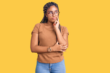Young african american woman with braids wearing casual clothes and glasses serious face thinking...