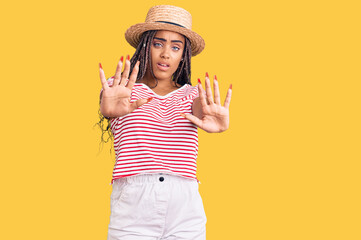 Fototapeta na wymiar Young african american woman with braids wearing summer hat doing stop gesture with hands palms, angry and frustration expression