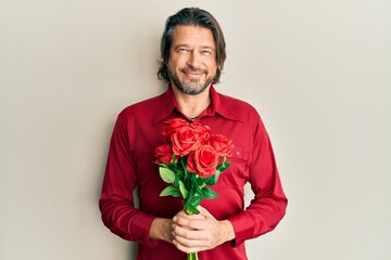 Middle age handsome man holding bouquet of red roses smiling with a happy and cool smile on face. showing teeth.