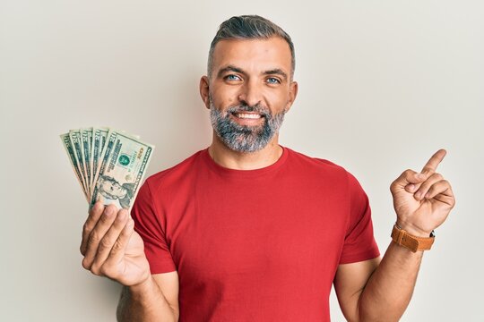 Middle age handsome man holding 20 dollars banknotes smiling happy pointing with hand and finger to the side