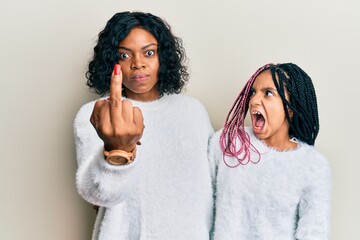 Beautiful african american mother and daughter wearing casual winter sweater showing middle finger,...