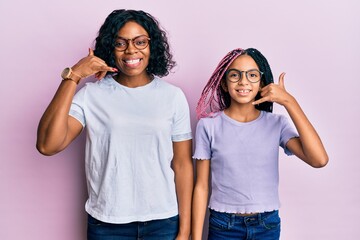 Beautiful african american mother and daughter wearing casual clothes and glasses smiling doing phone gesture with hand and fingers like talking on the telephone. communicating concepts.