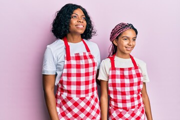 Beautiful african american mother and daughter wearing baker uniform looking to side, relax profile pose with natural face and confident smile.