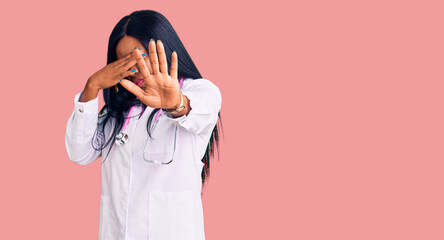 Young african american woman wearing doctor stethoscope covering eyes with hands and doing stop gesture with sad and fear expression. embarrassed and negative concept.