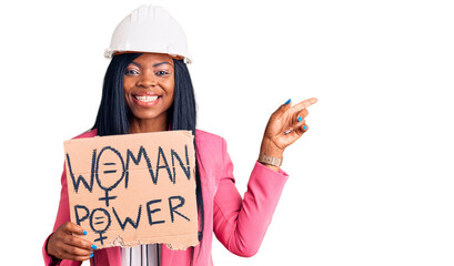 Young african american woman wearing architect helmet holding woman power banner smiling happy pointing with hand and finger to the side