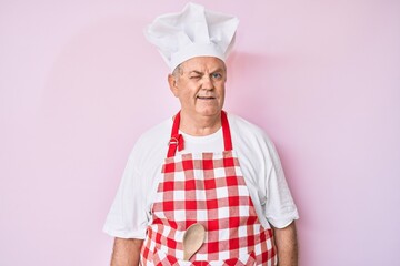 Senior grey-haired man wearing professional baker apron winking looking at the camera with sexy...