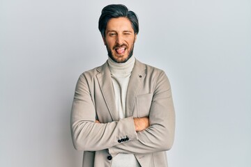 Young hispanic man with arms crossed gesture sticking tongue out happy with funny expression.