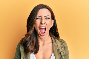 Young brunette woman wearing casual clothes over yellow background angry and mad screaming frustrated and furious, shouting with anger. rage and aggressive concept.