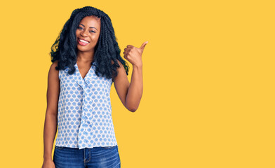 Beautiful african american woman wearing casual summer shirt smiling with happy face looking and pointing to the side with thumb up.