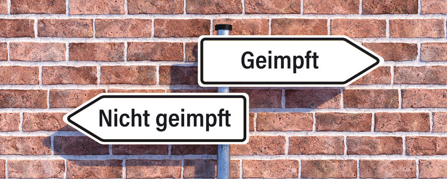 street sign with German message for VACCINATED and a crossed NOT VACCINATED in front of a brick wall