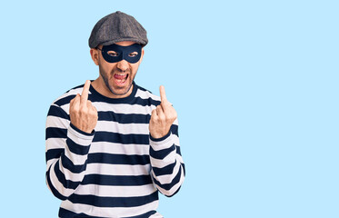 Young handsome man wearing burglar mask showing middle finger doing fuck you bad expression,...