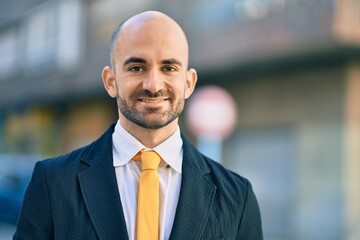 Fototapeta premium Young hispanic bald businessman smiling happy standing at the city.