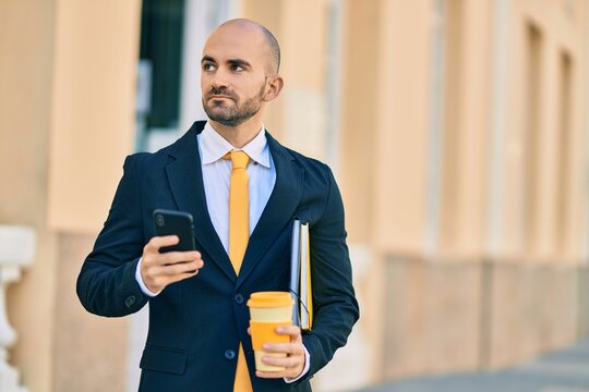 Young hispanic bald businessman with serious expression using smartphone drinking coffee at the city.