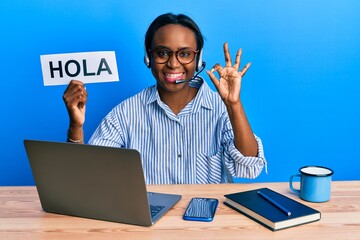 Young african woman wearing operator headset holding hola word doing ok sign with fingers, smiling friendly gesturing excellent symbol © Krakenimages.com