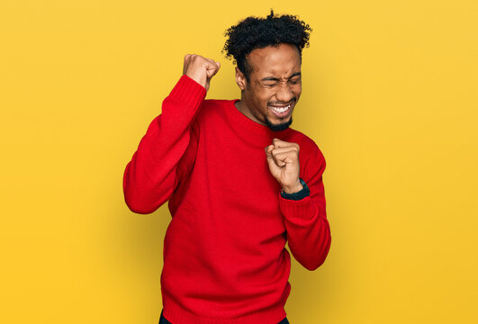 Young african american man with beard wearing casual winter sweater celebrating surprised and amazed for success with arms raised and eyes closed. winner concept.