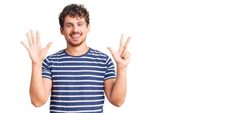 Young handsome man with curly hair wearing casual clothes showing and pointing up with fingers number eight while smiling confident and happy.