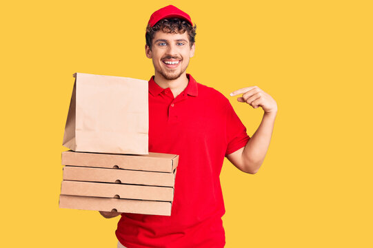 Young handsome man with curly hair holding delivery pizza box pointing finger to one self smiling happy and proud