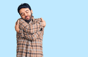 Young hispanic man wearing casual clothes hugging oneself happy and positive, smiling confident....