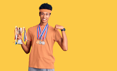 Young african american man holding champion trophy wearing medals pointing finger to one self smiling happy and proud