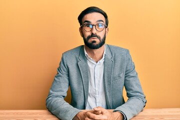 Young hispanic man working at the office puffing cheeks with funny face. mouth inflated with air,...