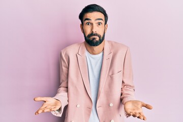 Young hispanic man wearing business jacket clueless and confused expression with arms and hands...