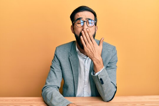 Young hispanic man working at the office bored yawning tired covering mouth with hand. restless and sleepiness.