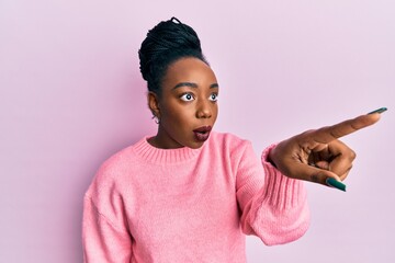 Young african american woman wearing casual winter sweater pointing with finger surprised ahead, open mouth amazed expression, something on the front