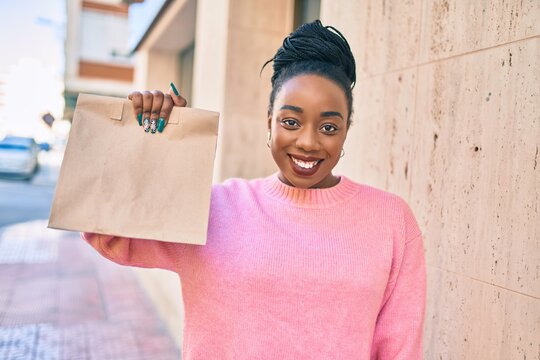 Young african american woman smiling happy holding delivery paper bag with take away food at the city.