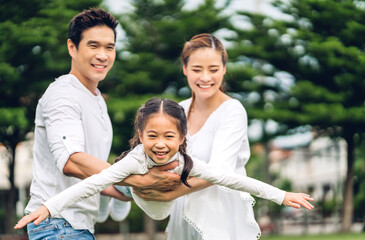 Portrait of enjoy happy love asian family father and mother carrying little child asian girl daughter flying on arms smiling playing and having fun moments good time in summer park at home