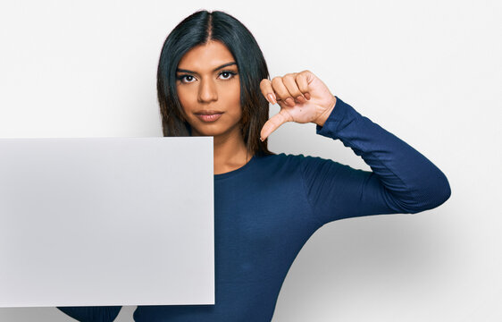 Young latin transsexual transgender woman holding blank empty banner with angry face, negative sign showing dislike with thumbs down, rejection concept