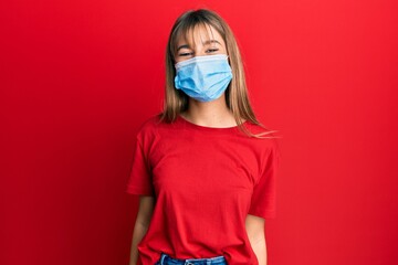 Teenager caucasian girl wearing medical mask looking positive and happy standing and smiling with a confident smile showing teeth