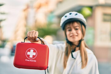 Caucasian sporty teenager girl wearing bike helmet holding first aid kit at the city.