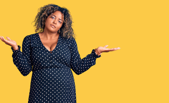 Young african american plus size woman wearing casual clothes clueless and confused expression with arms and hands raised. doubt concept.