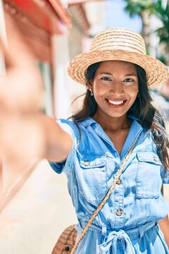 Young beautiful indian woman wearing summer hat smiling happy making selfie by the camera at the city.