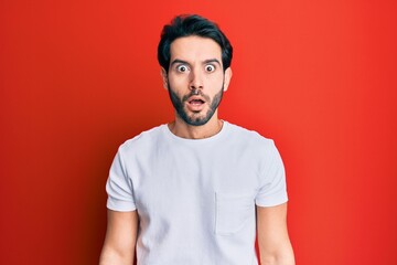 Young hispanic man wearing casual white tshirt afraid and shocked with surprise and amazed expression, fear and excited face.