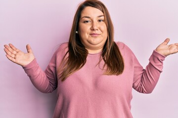 Fototapeta premium Beautiful brunette plus size woman wearing casual winter sweater clueless and confused with open arms, no idea and doubtful face.