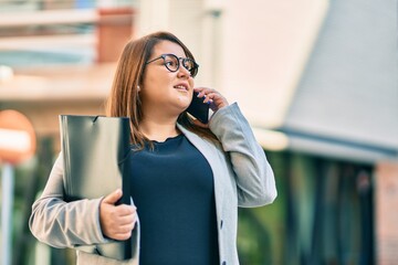 Young plus size businesswoman talking on the smartphone holding binder at the city.