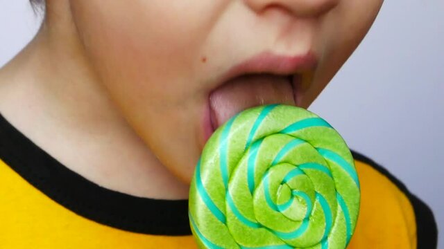 Close-up of a lower part of a face of a little boy licking a big twisted green-blue lollipop