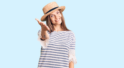 Fototapeta premium Beautiful caucasian woman wearing summer hat smiling friendly offering handshake as greeting and welcoming. successful business.