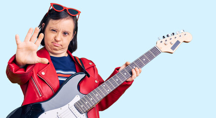 Obraz premium Brunette woman with down syndrome playing electric guitar with open hand doing stop sign with serious and confident expression, defense gesture