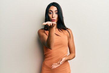 Beautiful hispanic woman wearing summer dress looking at the camera blowing a kiss with hand on air...