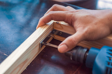 Woodworking with a drill to screw angle bracket in a wooden block with wood shavings and smoke in a woodworking workshop close-up power tool