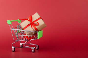 Gift box with red ribbon in mini grocery cart on pink background