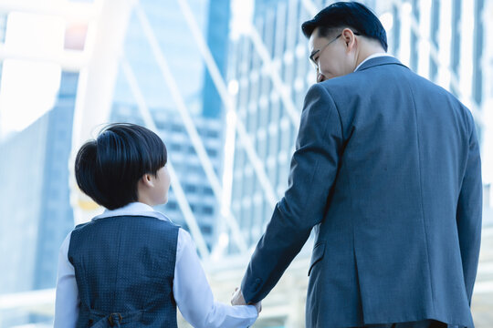 Happy Child Holding Fathers Hand With Love And Happiness Little Business Child Look At Dad And Walking Back To Their Home Together After They Travel Together With City Background. Happy Family Concept