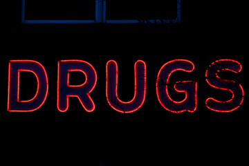 Drugs Neon sign in dark with tree in foreground