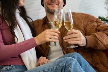 Couple celebrating holiday at home together. Sitting on sofa in sweaters and drinking champagne.